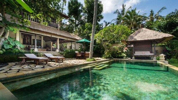 A pool area with lounge chairs, a thatched-roof structure, and lush tropical vegetation. - 2BR Family Villa – Pool & Garden View (Sayan)
