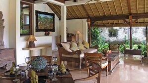 A spacious living area with a high ceiling, a dining table set with glassware and plates, and a comfortable seating arrangement. - 2BR Family Villa – Pool & Garden View (Sayan)