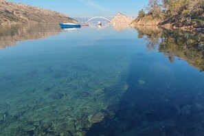 A clear lake with boats, a bridge, and rocky terrain.