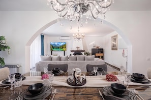 A modern living room with a dining area, a chandelier, and a television.