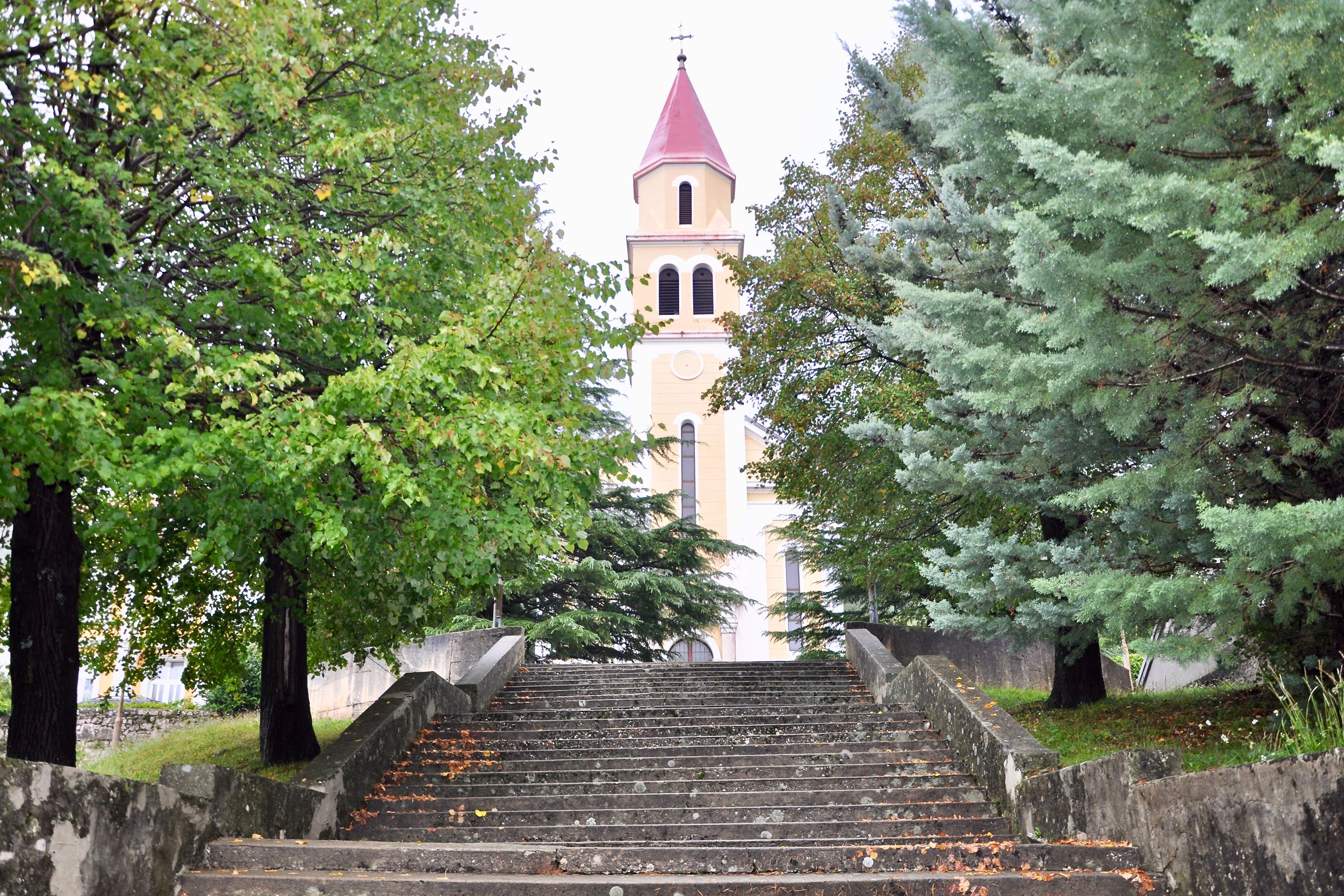 A set of stone steps leading up to a church with a red roof and a bell tower.