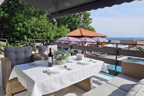 An outdoor dining area with a table set for two, surrounded by wicker furniture, a pool, and a view of the sea. - Villa Natali With Pool And Sea View (Kraljevica)