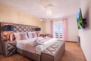 A modern hotel room with a large bed, a chandelier, a flat-screen TV, and a view of a mountainous landscape. - Villa Natali With Pool And Sea View (Kraljevica)