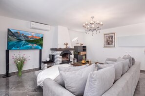 A modern living room with a flat-screen TV, a fireplace, a chandelier, and a grey sofa. - Villa Natali With Pool And Sea View (Kraljevica)