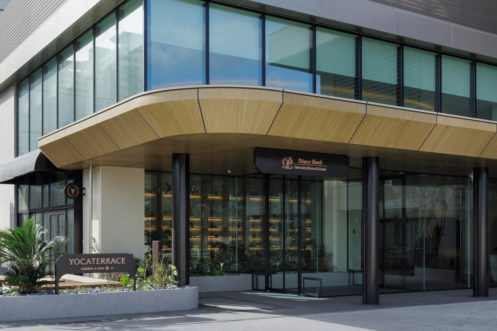 A modern hotel entrance with a curved roof, glass facade, and a sign for 'Prince Hotel.'