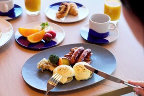Ein Frühstückstisch mit Tellern voller Speisen, einer Kaffeetasse und einem Glas Orangensaft.