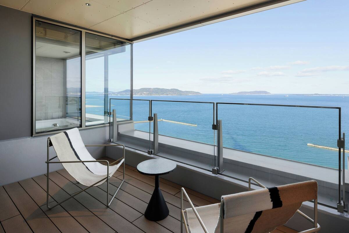 Ein Balkon mit zwei Liegestühlen, einem kleinen runden Tisch und einem Glasgeländer mit Blick auf das Meer.