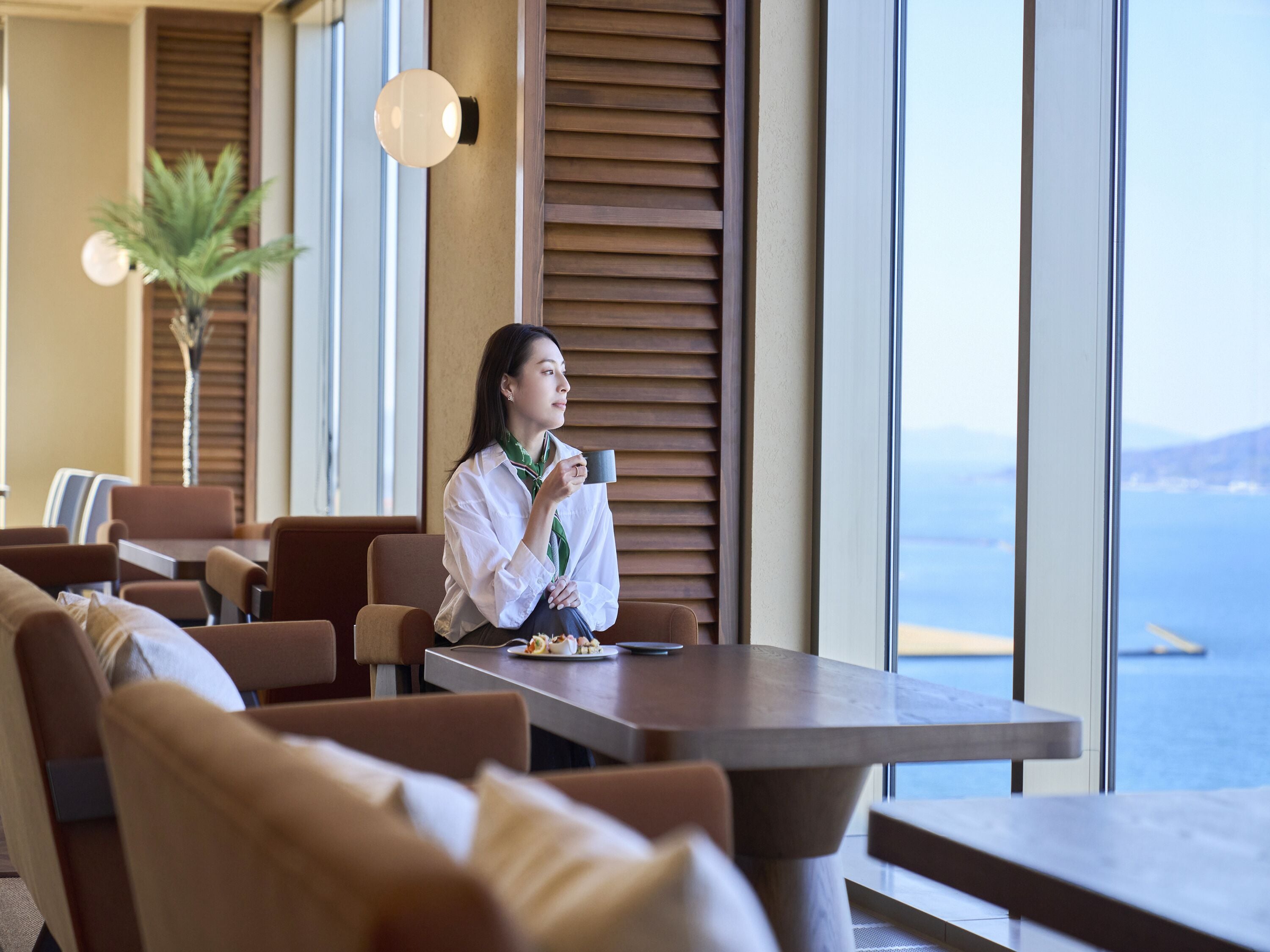 A modern hotel room with a large window, a dining table, and comfortable seating.