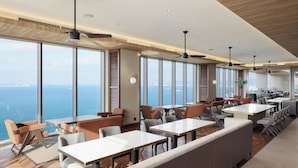 A modern dining area with high ceilings, large windows, and a view of the sea. - Fukuoka Prince Hotel Momochihama (Fukuoka)