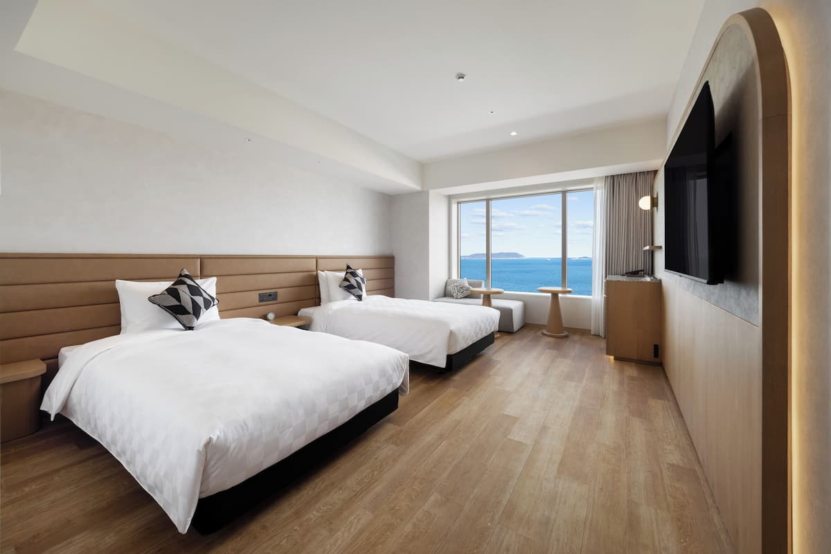 Ein Hotelzimmer mit zwei Betten, einem Fernseher, einem großen Fenster mit Blick und einem Holzboden.