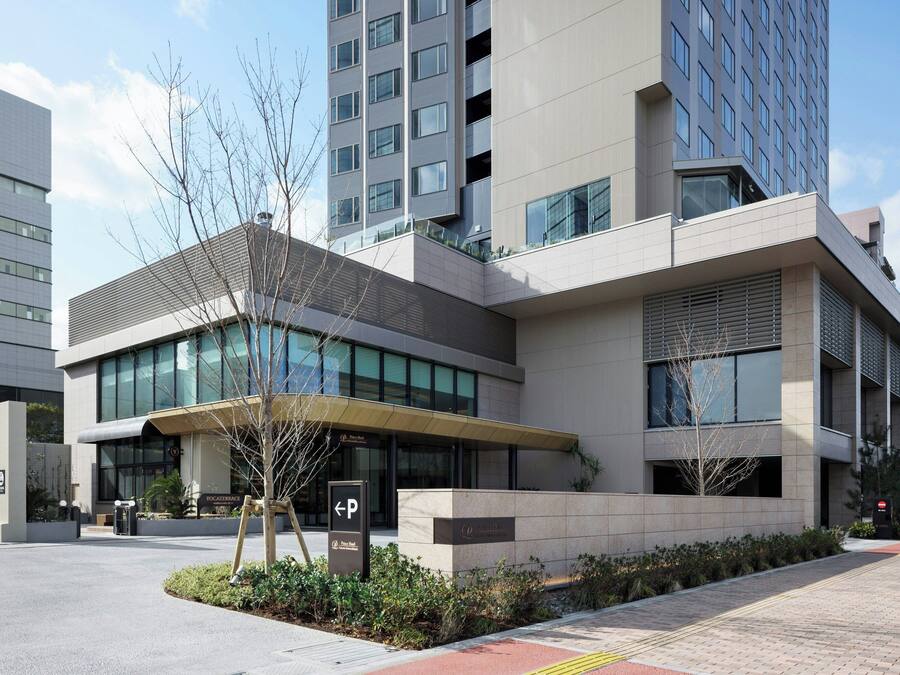 A modern building with a glass facade, a parking entrance, and a landscaped area with trees.
