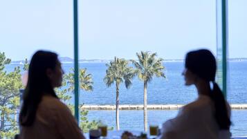 Two individuals seated at a table with a view of the sea and palm trees through large windows.