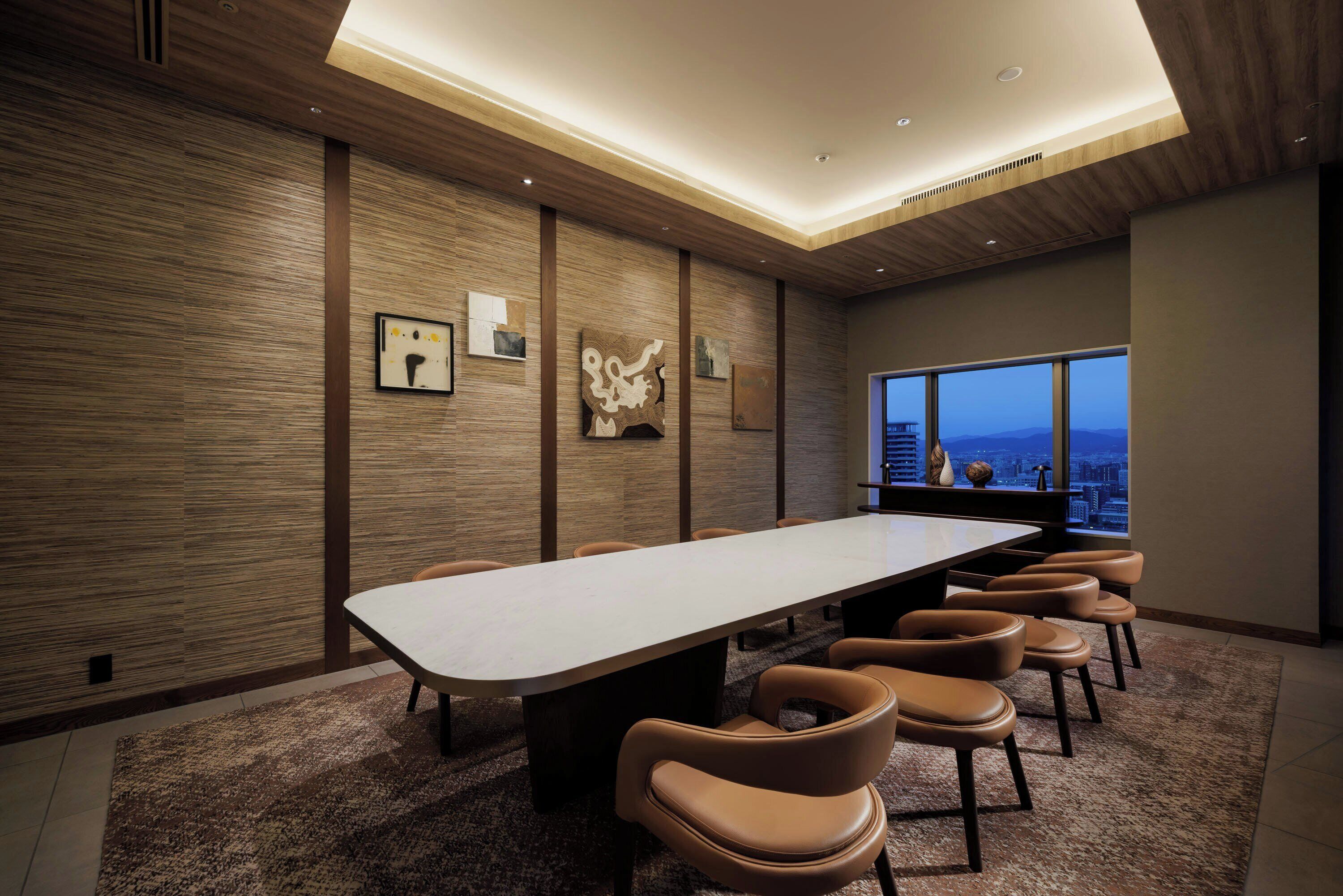 A conference room with a long table, several chairs, wooden panel walls, and a large window with a city view.