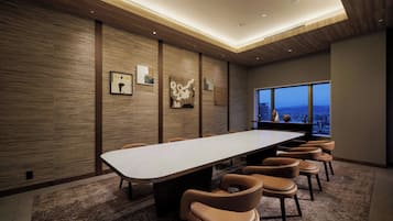 A conference room with a long table, several chairs, wooden panel walls, and a large window with a city view.