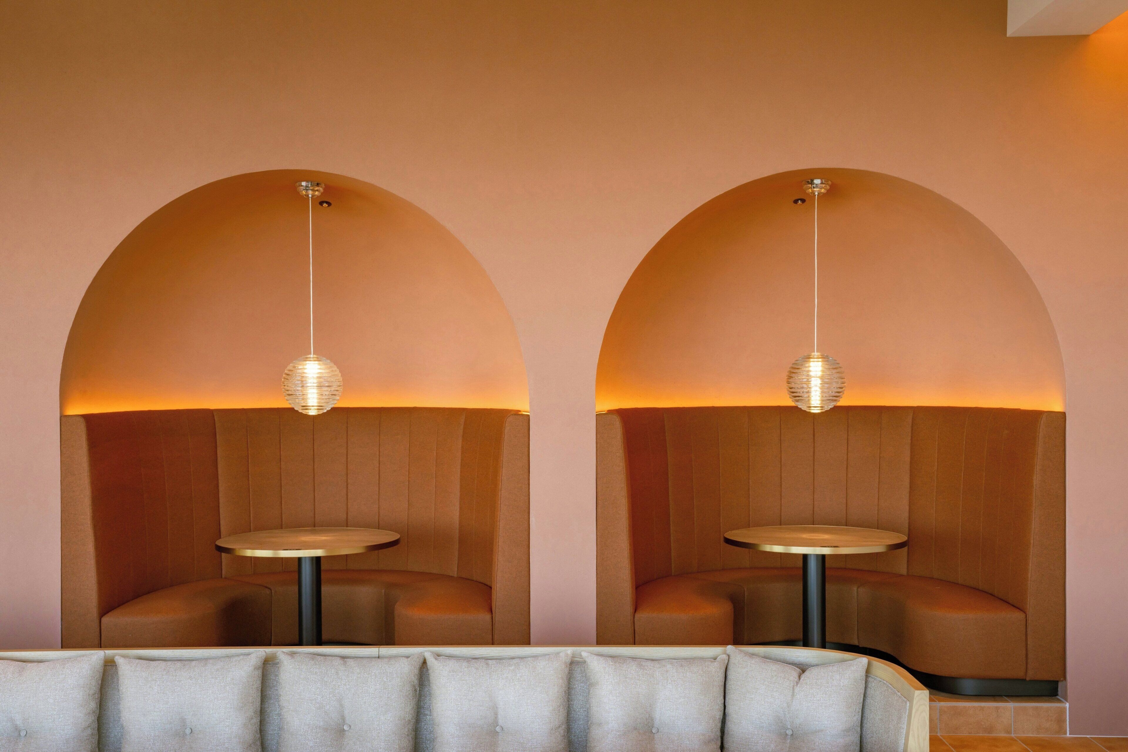 A modern interior with two arched seating areas, each with a round table and pendant lighting.
