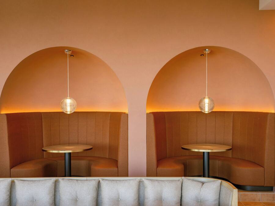 A modern interior with two arched seating areas, each with a round table and pendant lighting.