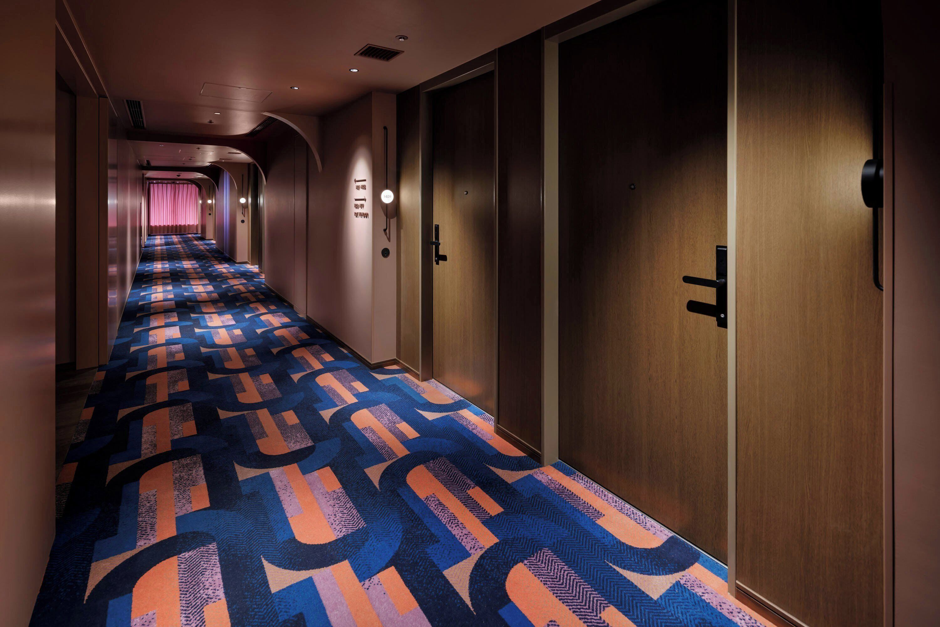 A hotel corridor with patterned carpet, wooden doors, and a long hallway.
