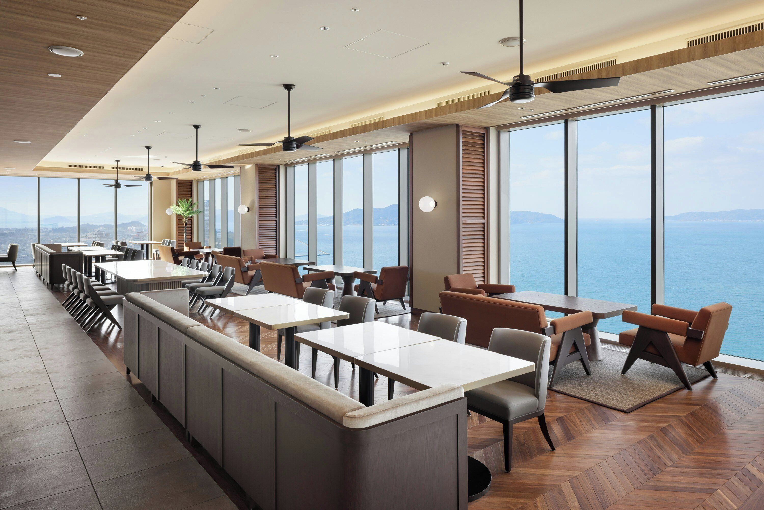 Een modern restaurant met hoge plafonds, grote ramen en uitzicht op zee.