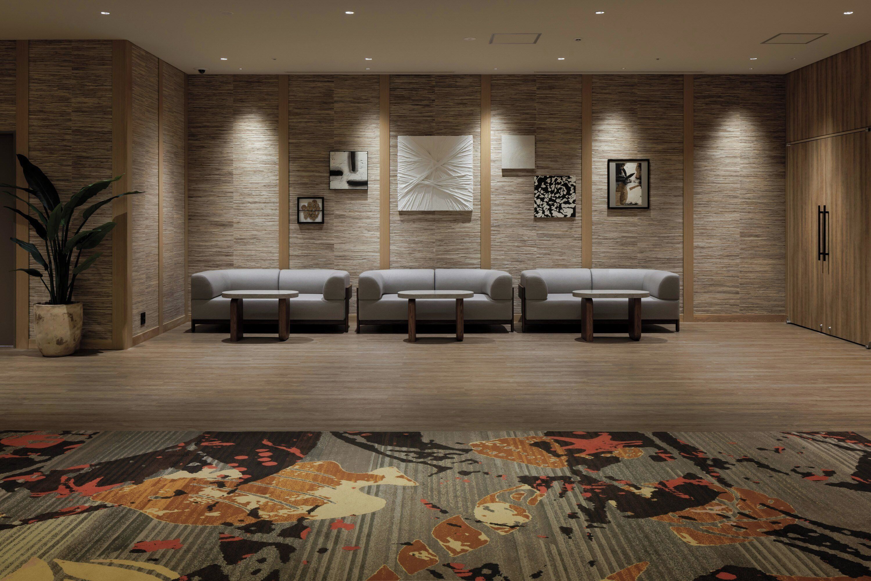 A modern hotel lobby with three sofas, a patterned carpet, and wooden panel walls.