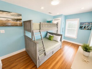 A bunk bed with a ladder, a window with blinds, and a painting on the wall.