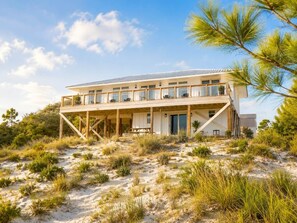 A beachfront property with a two-story structure, a covered patio, and a sandy landscape.