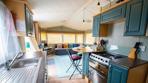 Une cuisine compacte équipée d’un évier, d’une cuisinière et d’armoires de couleur turquoise. On y trouve également un coin repas avec une table et des chaises.