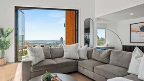 A modern living room with a large sectional sofa, a coffee table, and a view through a glass door to the outdoors.