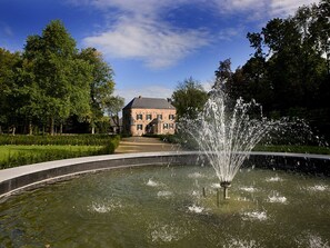 Surrounded by lush greenery, this historic building features a serene fountain and a stately facade.