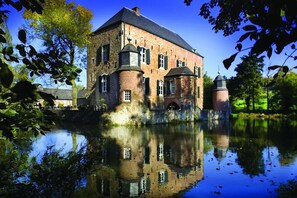 Stately brick building with a prominent tower, situated beside a serene body of water.
