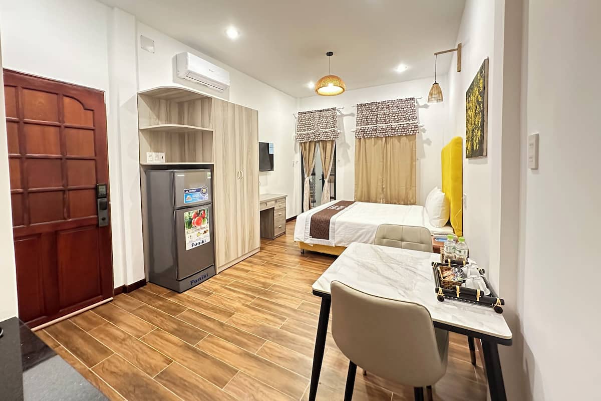 A compact hotel room with a kitchenette, a bed, a desk with a chair, and a dining table.