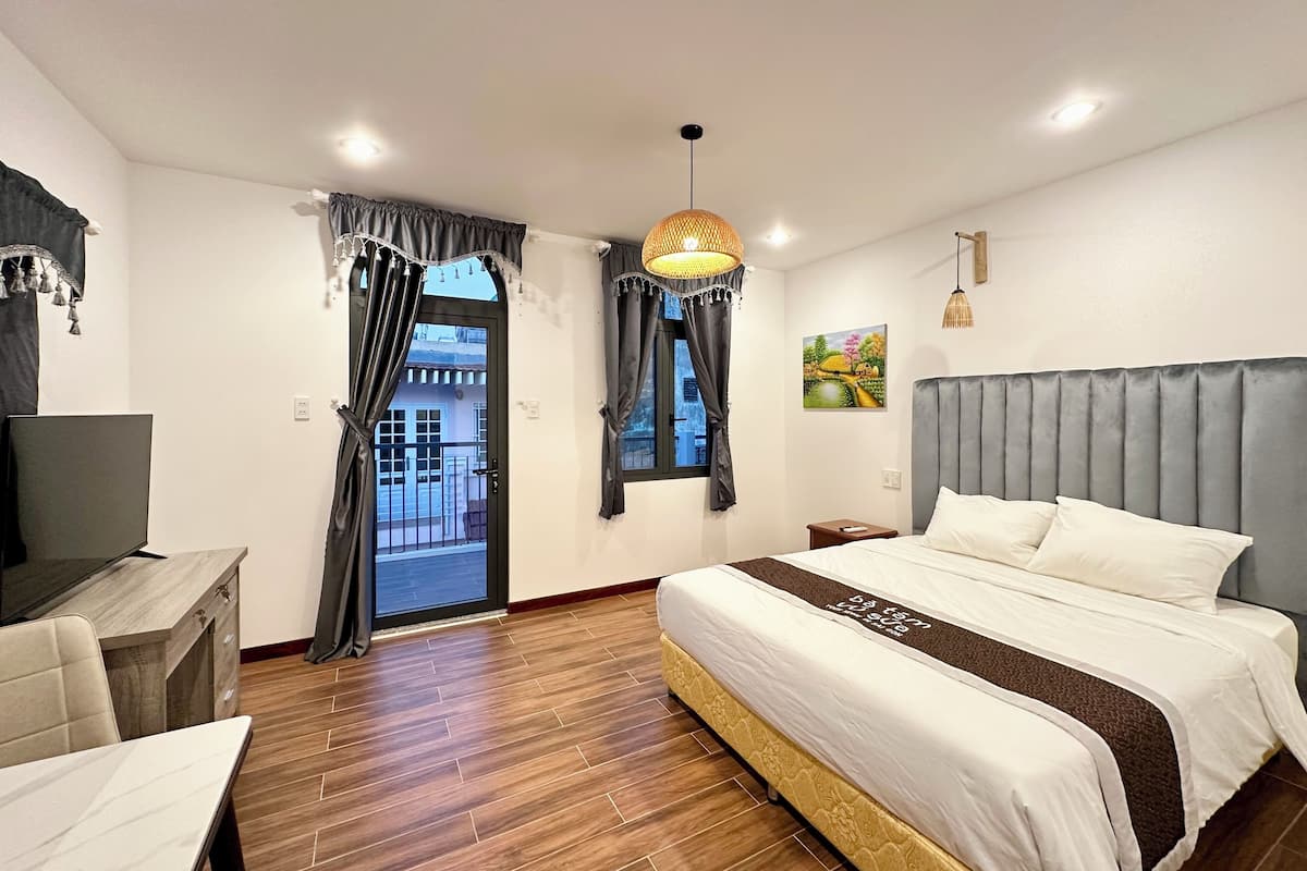 A hotel room with a large bed, a desk, and a balcony view.