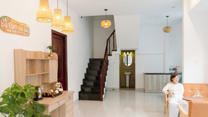 A modern interior with a wooden reception desk, a staircase, and a seating area with a person. - Ba Tam Vu Sua (Ho Chi Minh City)