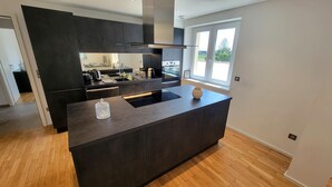 Une cuisine moderne avec des meubles de couleur sombre, un îlot central et une grande fenêtre qui laisse entrer la lumière naturelle.