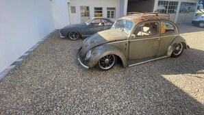 Une voiture ancienne est garée devant une maison dont le toit est recouvert de tuiles et qui possède un garage.