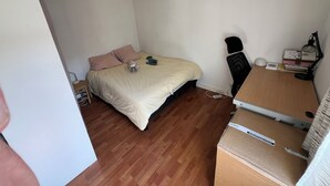 Et soveværelse med en seng, et skrivebord og en stol. Der er kasser på skrivebordet, og en lampe står på skrivebordet.