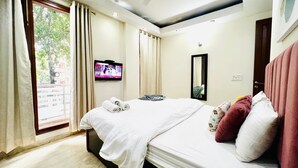 Una habitación de hotel con una cama grande, un televisor montado en la pared, una ventana con cortinas y una puerta.