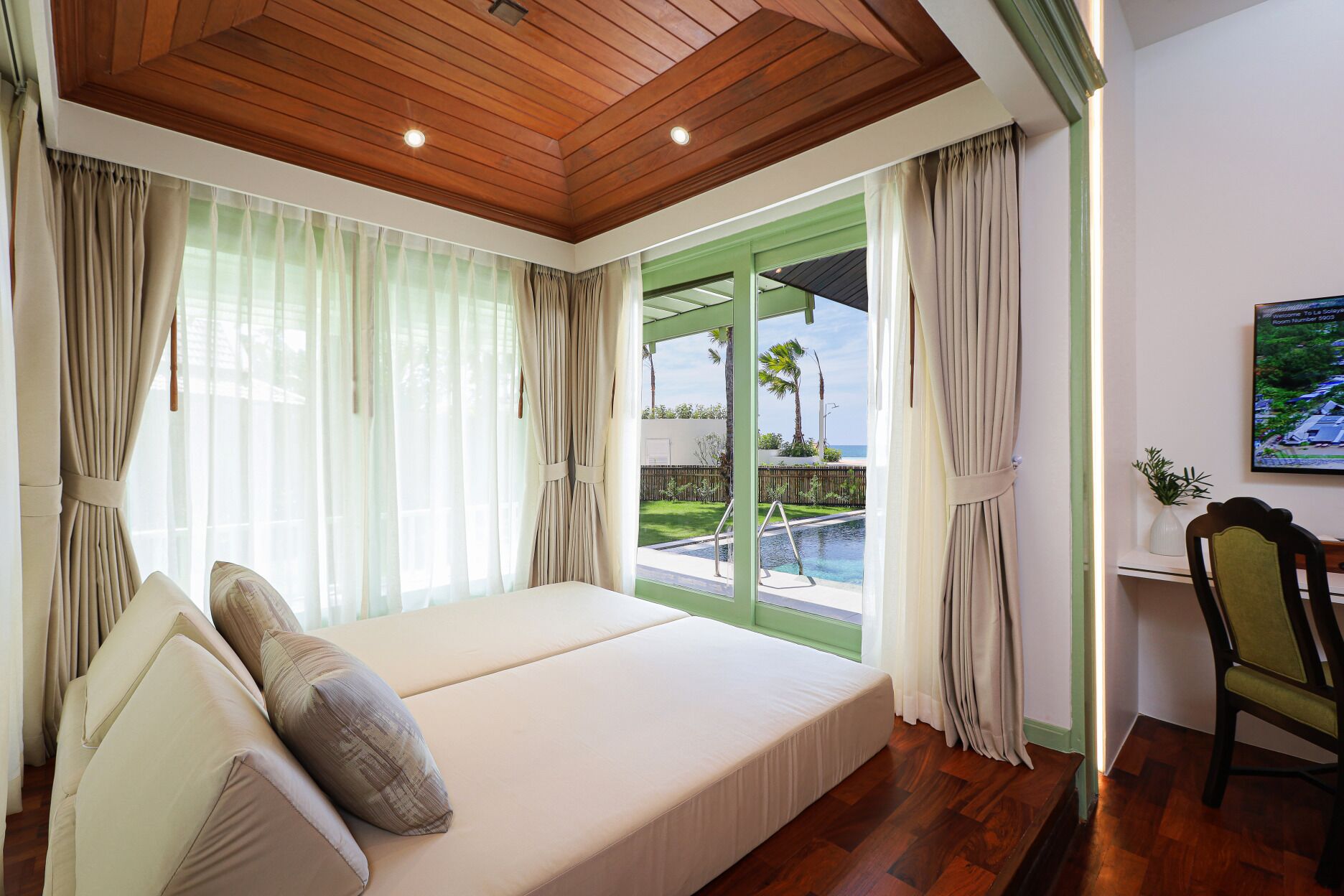 A bedroom with a large bed, a view of a pool, and a desk with a chair.