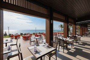 Un espace extérieur aménagé pour les repas, avec des tables et des chaises, offrant une vue sur la mer.