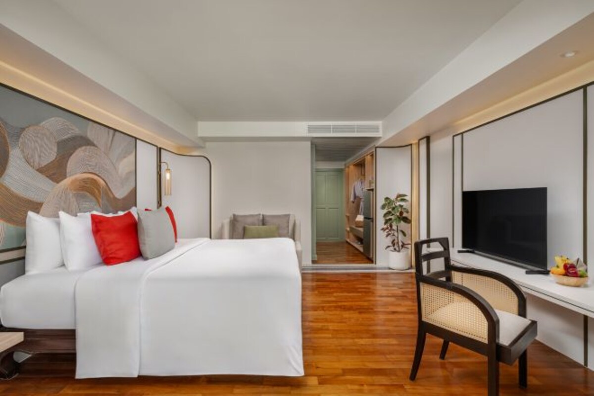 A hotel room with a bed, a desk with a TV, a chair, and a large painting on the wall.
