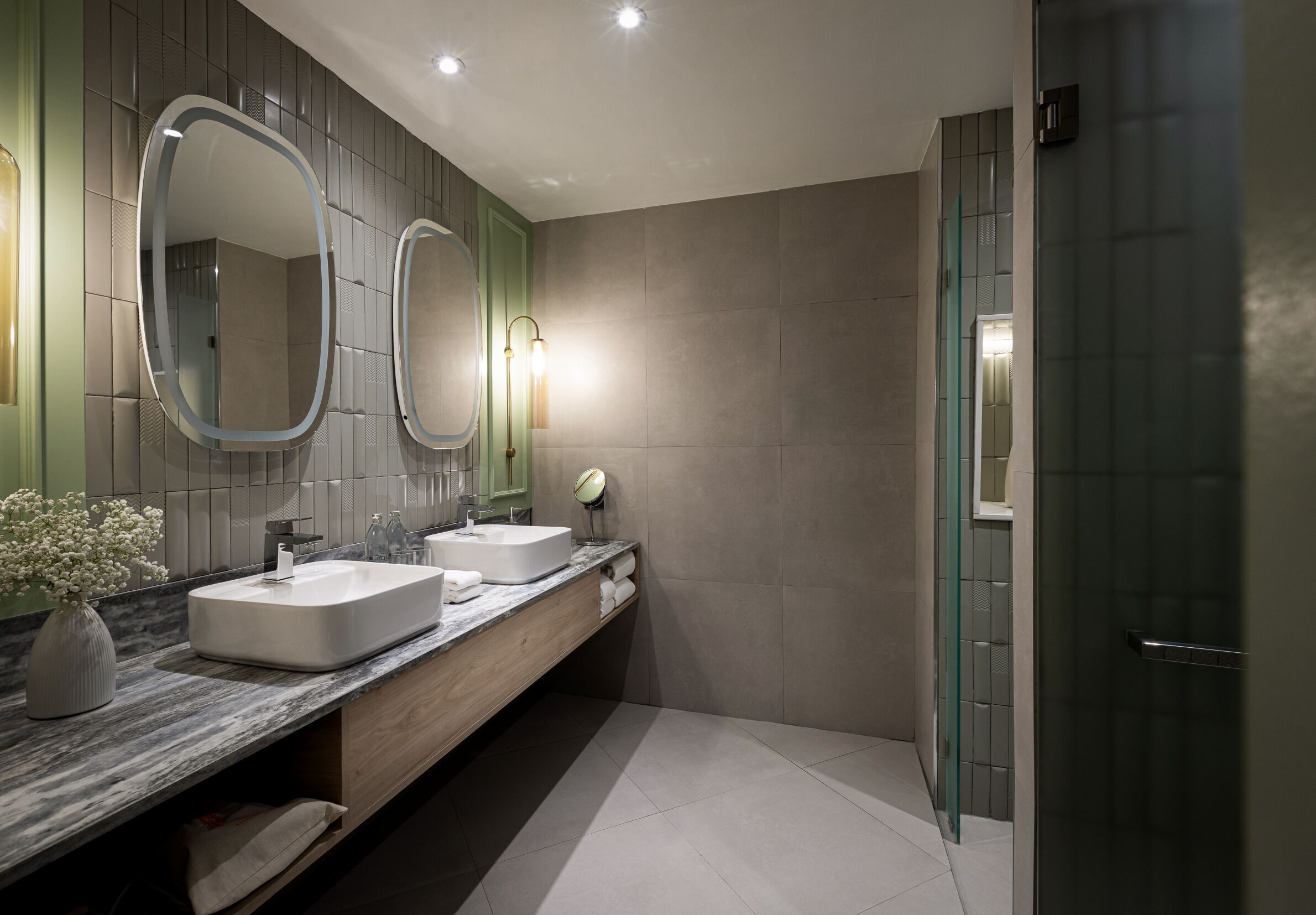 A modern bathroom with two sinks, a vanity, and a glass shower enclosure.