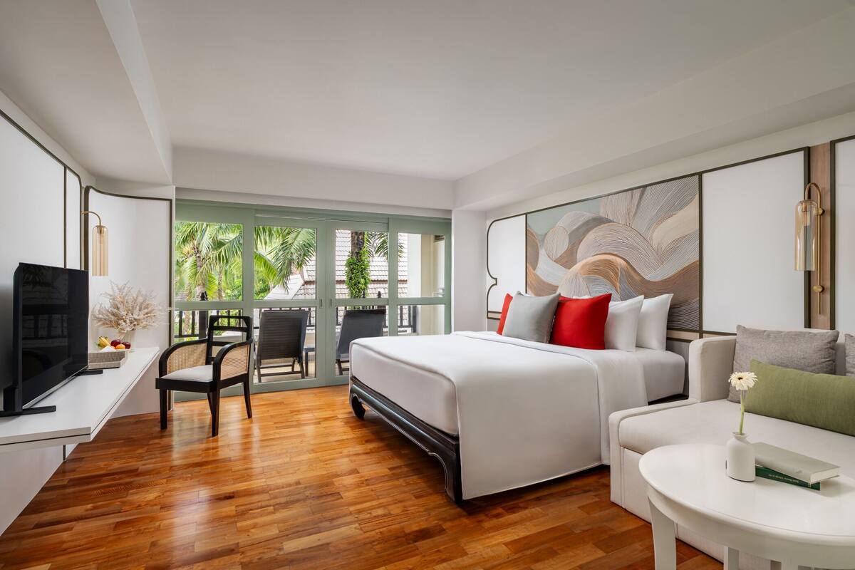 Habitación de hotel moderna con una cama, un escritorio con televisor, una silla y vistas a zonas verdes.