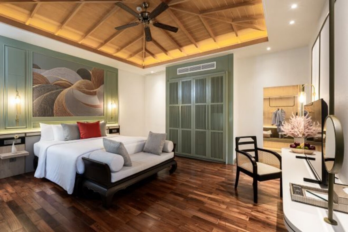 Ein modernes Schlafzimmer mit einem Bett, einem Sessel, einem Schminktisch mit Spiegel und einem Deckenventilator.
