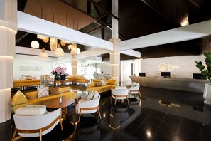 Un hall d’hôtel moderne comprenant un comptoir d’accueil, un espace détente avec des canapés et des fauteuils, et un éclairage décoratif.