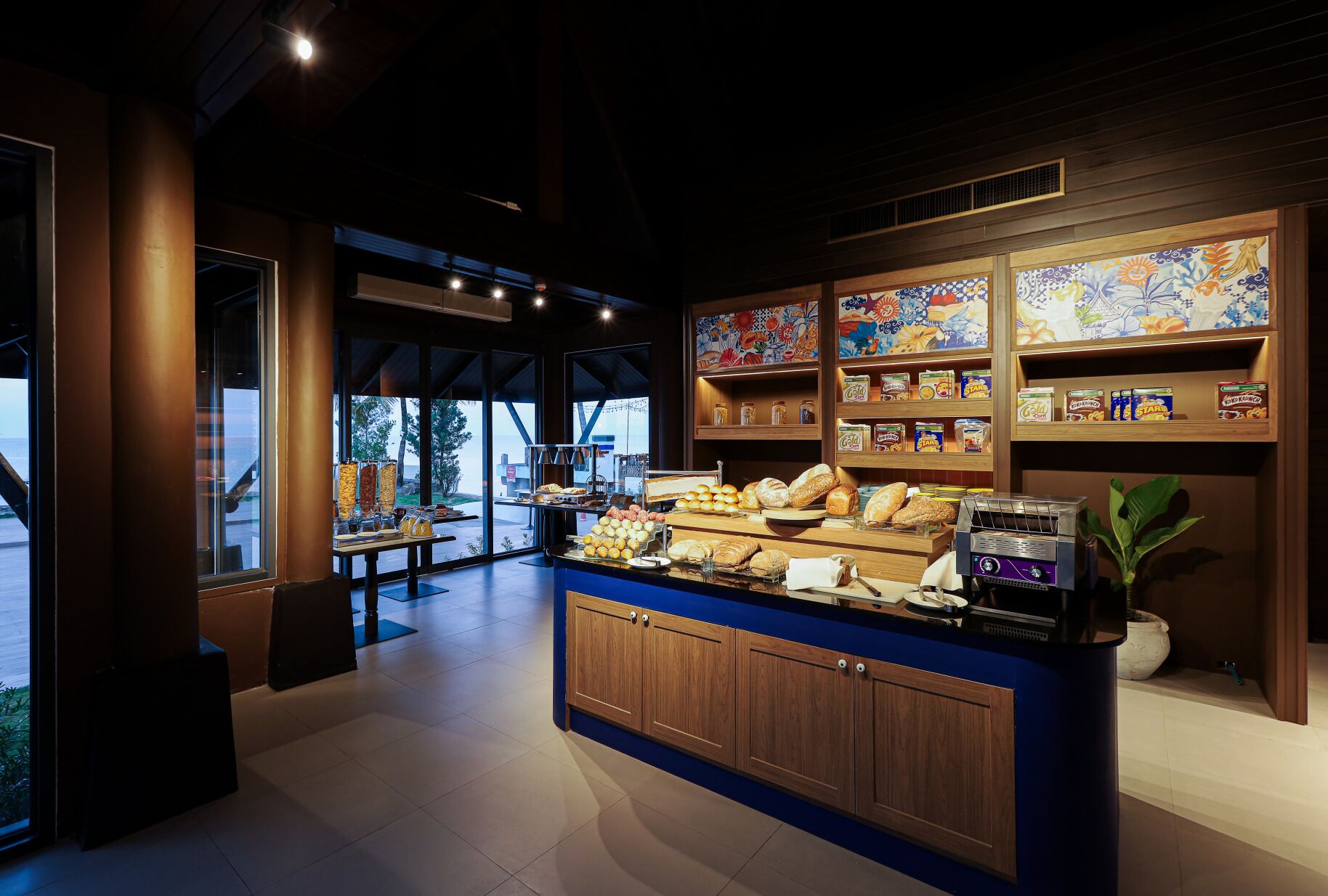 A bakery counter with various baked goods and a coffee machine, surrounded by shelves with jars and boxes.