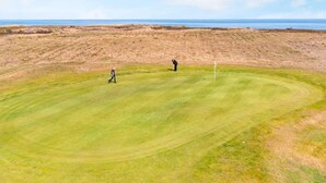 Un parcours de golf avec un mât de drapeau, un green d’entraînement et une zone d’herbe haute.