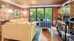 Interior acogedor de una cabaña con techo de madera, un sofá, una silla azul, una mesa de comedor y una chimenea.