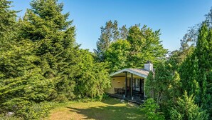 Una casita con porche cubierto, rodeada de un bosque frondoso.