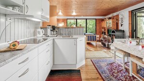 Una cocina moderna con armarios blancos, horno empotrado y un comedor con mesa y sillas de madera.