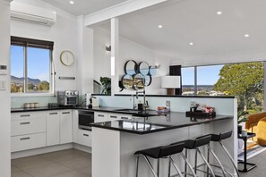 A modern kitchen with a central island, bar stools, and a view of the city. - Sanctuary 53 - Beautiful Views (Taupō)