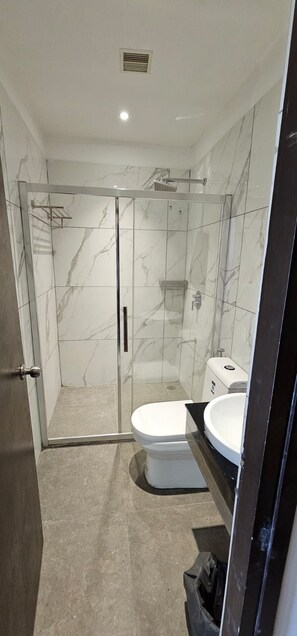 A modern bathroom with a glass-enclosed shower, a toilet, and a sink. - Park Niveda (Vijayawada)